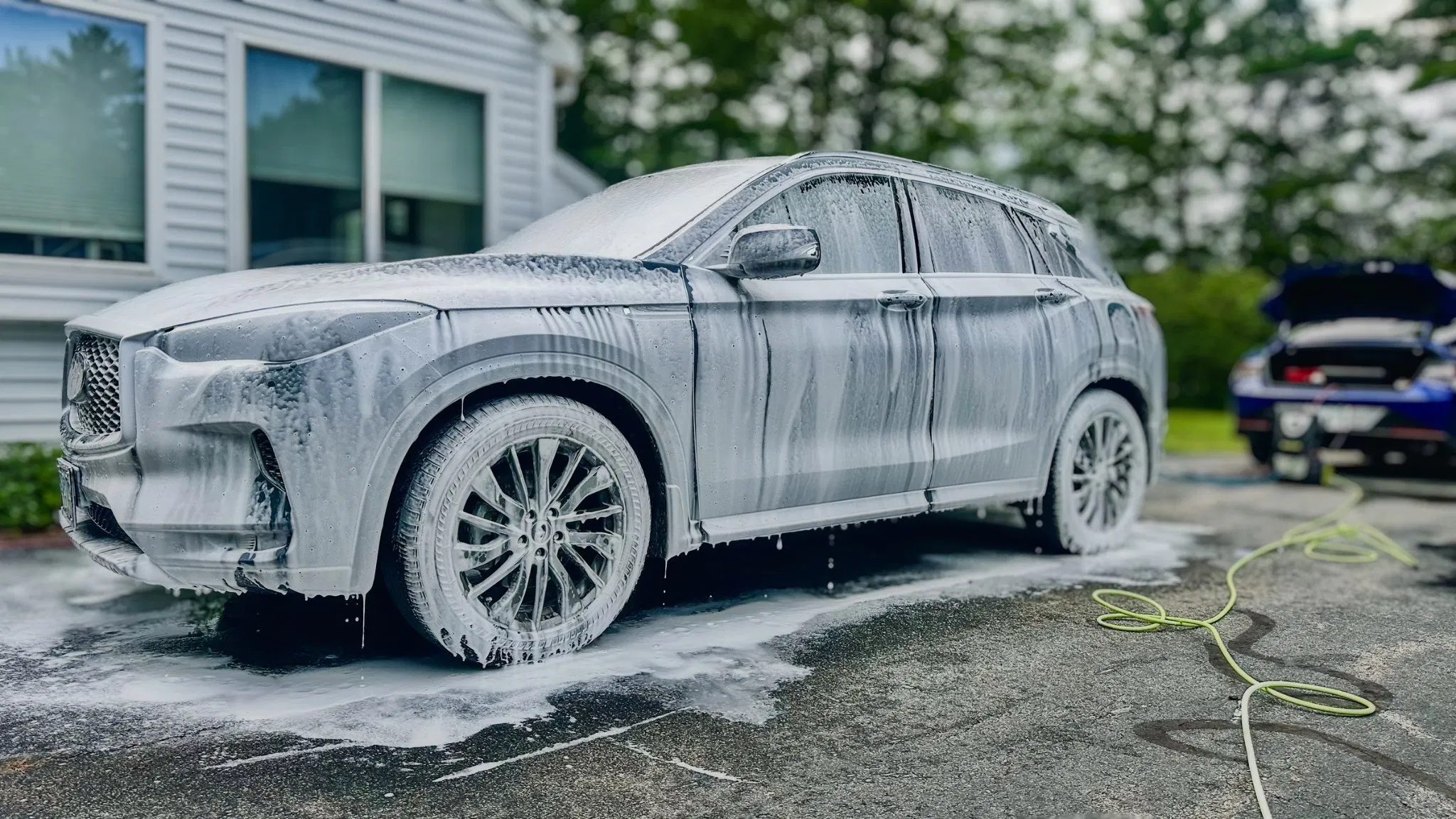 Blue SUV covered in foam during a mobile hand wash in a customer's driveway