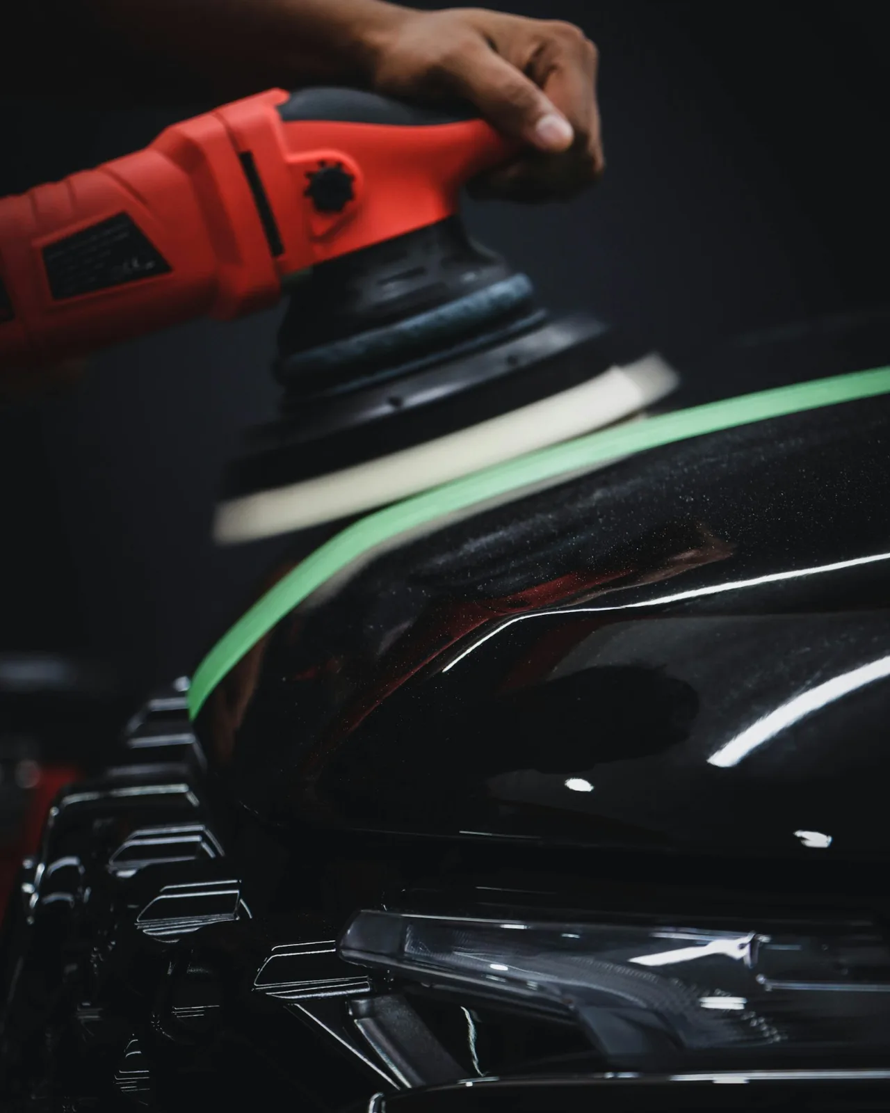 Dual-action polisher correcting black car paint next to a tape line